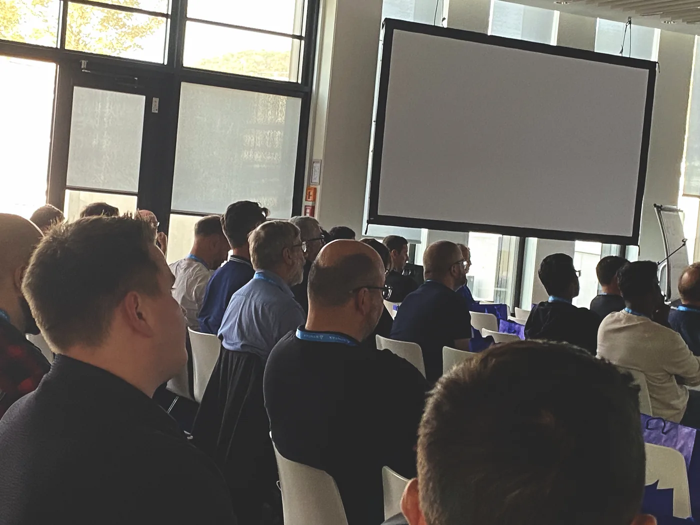 Attendees listening, lit by the tall windows along the side of the room